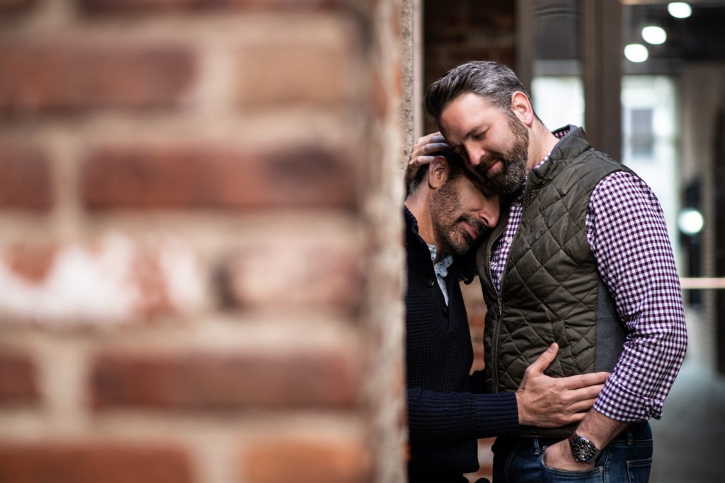 lgbtq couple leaning on brick wall