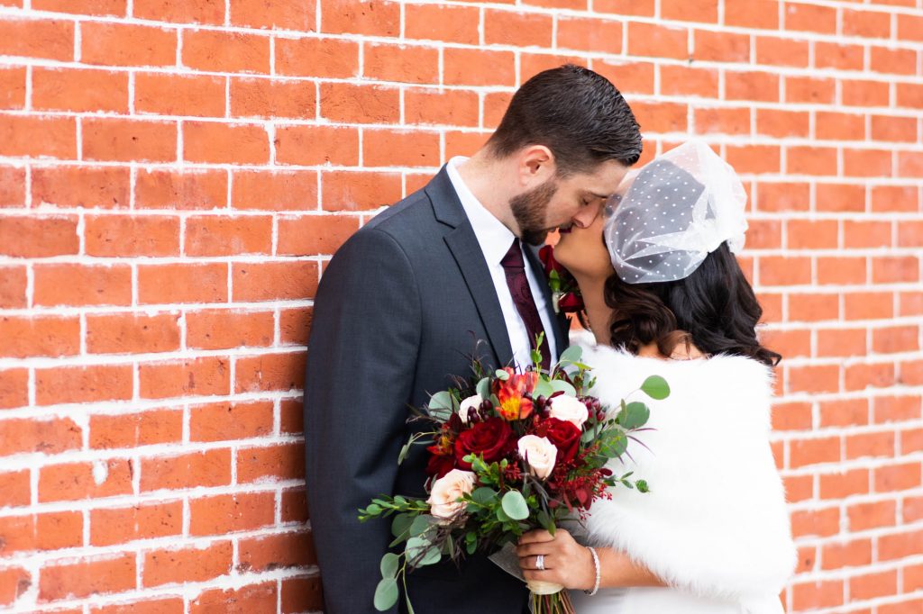 bride and groom against brick wall kissing